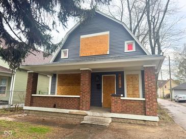 Two-story home with brick accents on the porch columns and boarded windows on a cloudy day at 3315 E Vermont St, Indianapolis, IN 46201