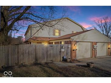 Exterior of the house with two garages and a fenced-in yard at dusk at 4814 Lynton Ct, Indianapolis, IN 46254