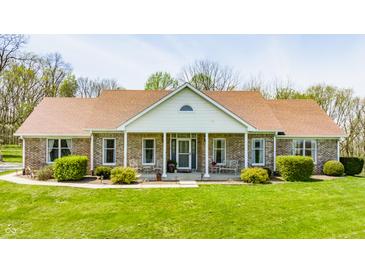 A charming single-story brick home features a well-manicured lawn and a cozy front porch with decorative chairs at 8654 N Baltimore Rd, Monrovia, IN 46157