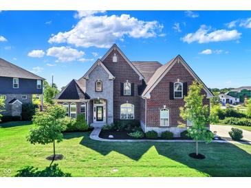 Imposing two-story brick home featuring a manicured lawn, arched windows, and stone accents under a partly cloudy sky at 3715 Kendall Wood Dr, Carmel, IN 46032