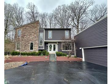 Striking two-story home featuring a blend of stone and contemporary siding, accentuated by mature trees and professional landscaping at 8224 Claridge Rd, Indianapolis, IN 46260