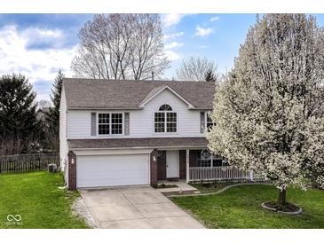 Charming two-story home with a well-manicured lawn, inviting porch, attached garage, and beautiful flowering trees at 8424 Nuckols Ln, Indianapolis, IN 46237