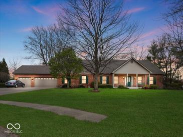 Charming brick home featuring an attached three-car garage, manicured lawn, and mature trees at dusk at 2810 Winterway Dr, Shelbyville, IN 46176