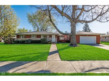 Charming brick home with a spacious front yard, mature tree, and attached two-car garage at 5124 Mccray St, Indianapolis, IN 46224