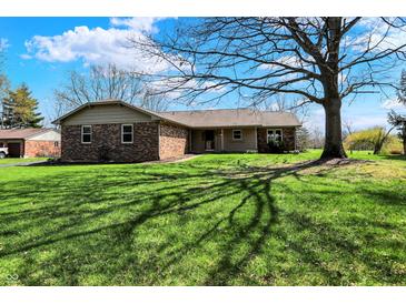 Ranch home with brick facade, green lawn, and mature tree casting shadows in a bright exterior shot at 3991 Clubhouse Dr, Greenfield, IN 46140