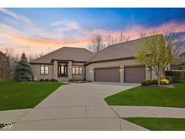 Beautiful brick home featuring a three-car garage, manicured lawn, and gorgeous landscaping at sunset at 6841 W Glory Maple Dr, McCordsville, IN 46055