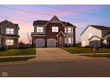 Beautiful two-story brick home with a two-car garage and manicured lawn, illuminated by the soft hues of twilight at 7128 English Oak Dr, McCordsville, IN 46055