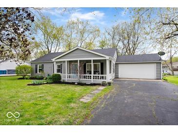 Charming single-story home with a well-manicured lawn, cozy porch, and attached garage at 7709 Lewis Rd, Indianapolis, IN 46256