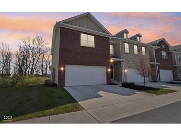 Two-story townhome featuring an attached garage, brick facade, and landscaped front yard under a warm sunset sky at 9725 Thorne Cliff Way # 105, Fishers, IN 46037
