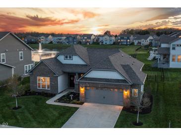 Stunning home with manicured lawn, gray brick, gray siding, 2-car garage and community pond view at sunset at 20515 Quicksilver Rd, Noblesville, IN 46062