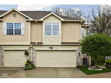 Charming townhome showcasing tan siding and a two-car garage, complemented by a well-manicured lawn and vibrant flower display at 1032 Grovewood Dr # 0, Beech Grove, IN 46107