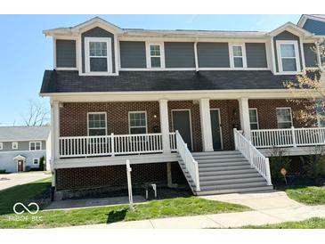 Inviting townhouse featuring a brick facade, white porch, and prominent staircase leading to the front entrance at 6157 Winthrop Ave, Indianapolis, IN 46220