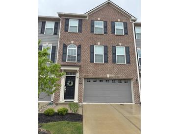 A three-story brick townhouse featuring black shutters, gray siding, and a gray garage door at 17364 Graley Pl, Westfield, IN 46074