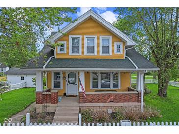 Charming yellow two-story home featuring a welcoming front porch with brick accents and a classic white picket fence at 25 N Wayburn St, Indianapolis, IN 46229