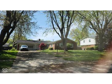 Charming one-story brick home with mature trees and a covered carport on a sunny day at 7629 Walton Dr, Indianapolis, IN 46214