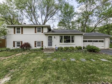 Classic white brick home featuring shuttered windows, a well-manicured lawn, and an attached two car garage at 7216 N Parker Ave, Indianapolis, IN 46240