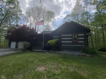 Beautiful log-cabin home featuring a covered porch with an American flag waving in a serene wooded setting at 7916 N Lasalle Rd, Morgantown, IN 46160