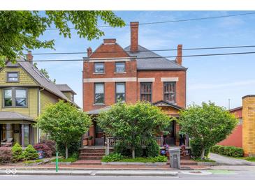 A stately brick home with mature trees, showcasing classic architecture under a clear sky at 419 N College Ave, Indianapolis, IN 46202
