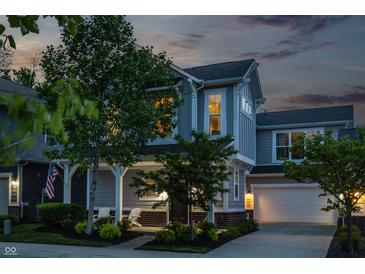 Charming two-story home featuring a covered front porch, attached garage, and well-manicured lawn at dusk at 7218 Antiquity Dr, Carmel, IN 46033