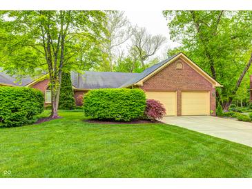 Charming brick home featuring a two-car garage and a lush green lawn surrounded by mature trees at 9324 W Point Pl, Indianapolis, IN 46268