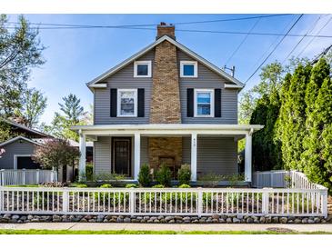 Charming two-story home featuring gray siding, brick chimney, a front porch, and a neatly manicured yard at 413 E 40Th St, Indianapolis, IN 46205