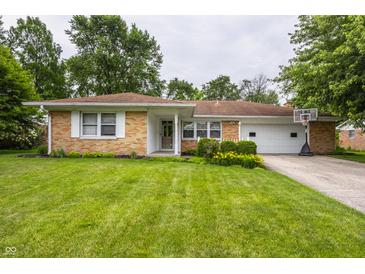Charming brick home featuring a well-manicured lawn, flower beds, and attached two-car garage with basketball hoop at 8103 Rumford Rd, Indianapolis, IN 46219