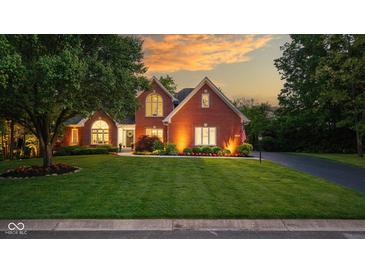 Charming brick home with a manicured lawn and beautiful landscaping, illuminated by warm exterior lighting at 11245 Old Stone Dr, Indianapolis, IN 46236