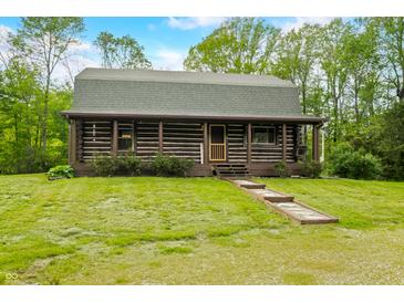 Charming log cabin featuring a cozy front porch, stone walkway, and well-maintained lawn with mature trees in a serene setting at 6968 S 300 W, Trafalgar, IN 46181