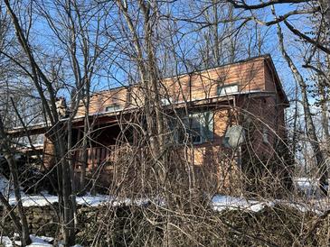 Cozy home with wood siding, complemented by bare winter trees, and a quaint front porch, set amongst an aged stone foundation at 8803 S Sleepy Hollow Rd, Waldron, IN 46182