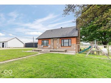Charming single-story home featuring orange siding, a stone chimney, and a spacious front lawn with a playground at 671 W 350 N, Shelbyville, IN 46176