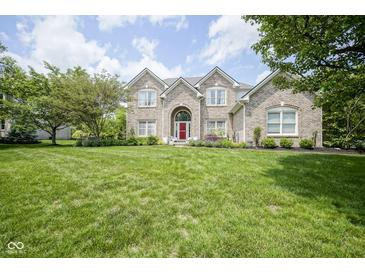 Stunning brick home featuring a large front yard, red door, and mature trees at 13244 Snow Owl Dr, Carmel, IN 46033