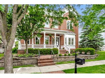 Inviting red brick home featuring a charming front porch, well-manicured lawn, and professional landscaping at 2037 Stanhope St, Carmel, IN 46032