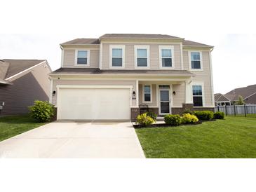 Two-story tan home featuring an attached two-car garage, front yard landscaping and a covered front entryway at 10447 Pintail Ln, Indianapolis, IN 46239