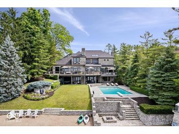 Stunning lakefront home featuring a pool, stone terrace, and lush landscaping with mature trees at 11715 Landings Dr, Indianapolis, IN 46256