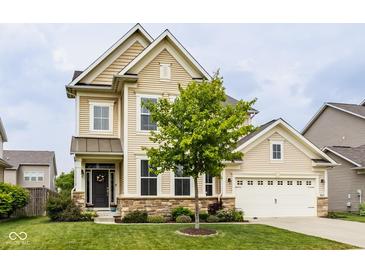 Charming two-story home with tan siding, stone accents, a well-manicured lawn, and lush landscaping at 7824 Hedgehop Dr, Zionsville, IN 46077