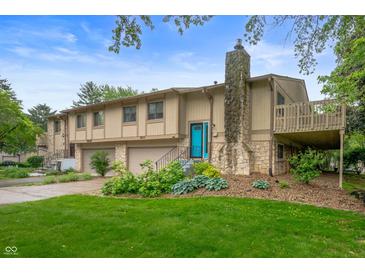 Two-story townhome with a stone chimney, a stone facade, attached garages, a deck, and a vibrant blue front door at 7831 Eagle Valley Pass, Indianapolis, IN 46214