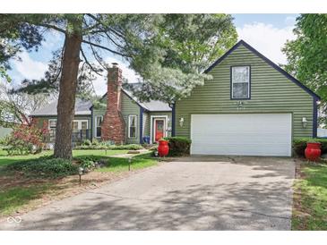 Exterior view of a charming green home with white garage door, red door and mature trees at 6210 Mckinley Ct, Indianapolis, IN 46220
