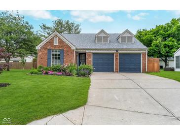 Charming brick home featuring a two-car garage, well-manicured lawn, and colorful flower beds at 6789 Passage Cir, Indianapolis, IN 46250