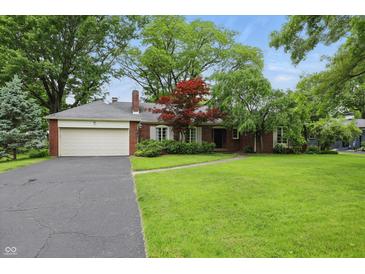Charming brick home featuring an attached two-car garage, lush green lawn, mature trees, and professionally landscaped garden at 8752 Washington Blvd E Dr, Indianapolis, IN 46240