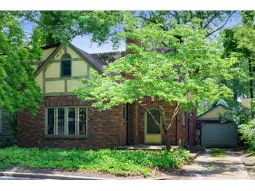 Charming brick home with an arched doorway, lush landscaping, and a detached garage at 521 Kessler Blvd E Dr, Indianapolis, IN 46220