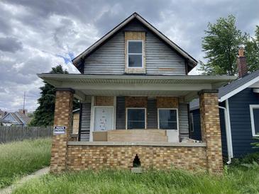 Exterior shot of a dilapidated home with a brick porch, boarded windows, and overgrown lawn at 243 Iowa St, Indianapolis, IN 46225