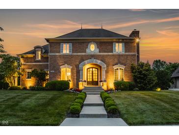 Charming two-story brick home with manicured lawn, elegant entrance, and warm exterior lighting at sunset at 6639 E Deerfield Dr, Zionsville, IN 46077