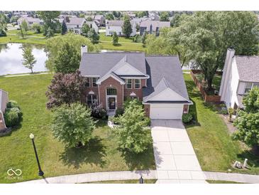 Beautiful brick home featuring mature landscaping, a spacious driveway, and picturesque pond views at 14353 Chariots Whisper Dr, Carmel, IN 46074
