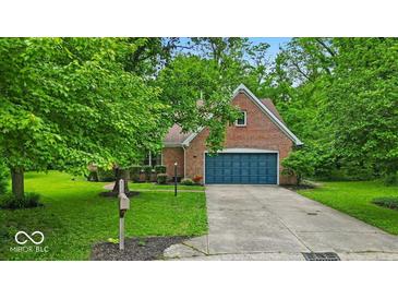 Charming brick home with a blue garage door, a well-manicured lawn, and mature trees providing shade at 5558 Spicebush Dr, Indianapolis, IN 46254