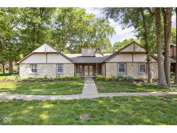 Charming stone home featuring mature trees, manicured lawn and a traditional American flag display at 2947 Talping Row, Indianapolis, IN 46268