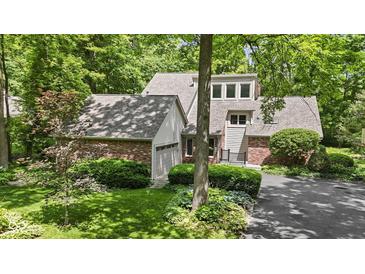 Brick home featuring an attached garage, manicured lawn, and lush landscaping at 7426 Shadow Wood Dr, Indianapolis, IN 46254