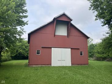 Red barn with white sliding doors and two windows is surrounded by a lush green lawn and trees at 18229 Moontown Rd, Noblesville, IN 46062