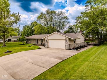 Charming single-story home featuring stone accents, a two-car garage, and a long driveway with lush landscaping at 7405 N Janna Dr, Muncie, IN 47303