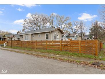 Tan home featuring a wood fence, well-maintained lawn, and tree line, all showcased under a bright, partly cloudy sky at 802 N Tuxedo St, Indianapolis, IN 46201