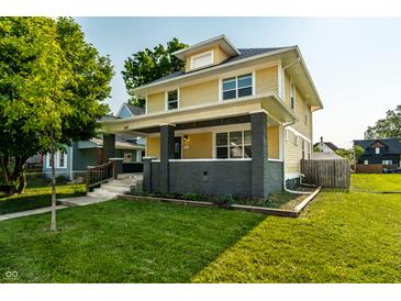 Charming yellow two-story home featuring a covered porch and a well-manicured front lawn on a sunny day at 805 N Temple Ave, Indianapolis, IN 46201